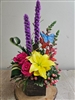 Rustic Springs arrangement with yellow lilies, pink roses, orange snapdragons, purple liatris, and hypericum berries in a cube vase with butterfly accent