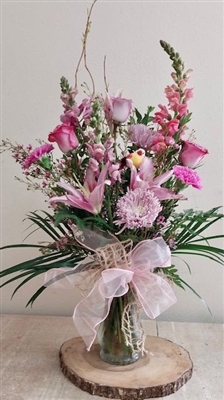 Pink and lavender bouquet with roses, lilies, carnations, spider mums, and snapdragons accented with a bird’s nest.