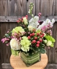 Blush and green garden-style bouquet with roses, carnations, hydrangea, hypericum berries, and stock in a leaf-lined glass cube.