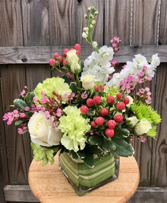 Blush and green garden-style bouquet with roses, carnations, hydrangea, hypericum berries, and stock in a leaf-lined glass cube.