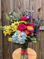 Colorful Wishes Bouquet with blue hydrangea hot pink roses yellow alstroemeria orange carnations blue delphinium purple statice and greenery in a clear glass vase