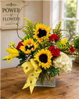 Sunflower and red rose bouquet with yellow lilies, white hydrangea, wax flower, and bee ribbon in a glass cube vase.