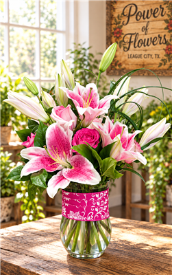 Pink Stargazer lily and rose bouquet in a clear glass vase with decorative pink ribbon