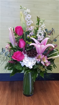 Fuchsia Lily and Rose bouquet with stargazer lilies, hot pink roses, pink larkspur, white hydrangea, alstroemeria, eucalyptus, and lotus pod in a clear cylinder vase
