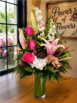Fuchsia Lily and Rose bouquet with stargazer lilies, hot pink roses, pink larkspur, white hydrangea, alstroemeria, eucalyptus, and lotus pod in a clear cylinder vase