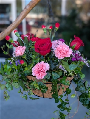 Hanging basket arrangement with trailing English ivy, red roses, pink and red carnations, purple statice, and red alstroemeria from Power of Flowers in League City, TX