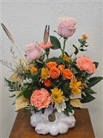 Blush roses, peach carnations, orange spray roses, yellow daisy mums, and limonium arranged in a hand-painted white pumpkin vase with gold stem.