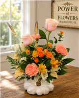 Blush roses, peach carnations, orange spray roses, yellow daisy mums, and limonium arranged in a hand-painted white pumpkin vase with gold stem.