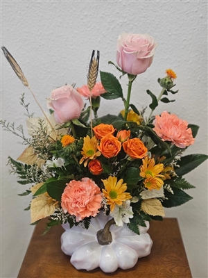 Blush roses, peach carnations, orange spray roses, yellow daisy mums, and limonium arranged in a hand-painted white pumpkin vase with gold stem.