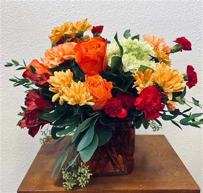 Orange and red bouquet with roses carnations alstroemeria and daisies in a glass vase