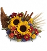 Autumn cornucopia centerpiece with sunflowers, orange roses, red and yellow mums, wheat, and cinnamon sticks.
