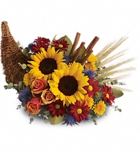 Autumn cornucopia centerpiece with sunflowers, orange roses, red and yellow mums, wheat, and cinnamon sticks.
