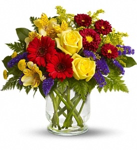 Sunny mixed bouquet with yellow roses, red gerbera-style blooms, purple statice, alstroemeria, and greenery in a clear vase
