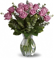 Dozen lavender roses arranged with eucalyptus and greenery in a clear glass vase.