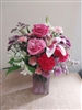 All-around bouquet in a clear vase with pink roses, lavender Fuji mums, pink alstroemeria, Bells of Ireland, green button mums, and pink carnations â€” approx. 11" x 13".
