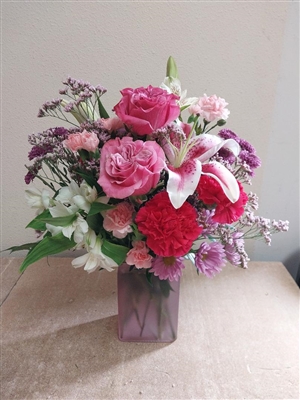 All-around bouquet in a clear vase with pink roses, lavender Fuji mums, pink alstroemeria, Bells of Ireland, green button mums, and pink carnations â€” approx. 11" x 13".