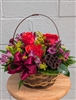 Autumn basket arrangement with orange roses, purple alstroemeria, burgundy button mums, solidago, greenery, and a lotus pod with a berry bow.