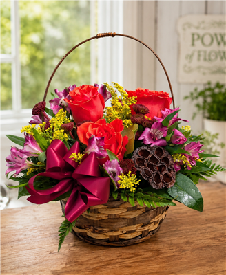 Autumn basket arrangement with orange roses, purple alstroemeria, burgundy button mums, solidago, greenery, and a lotus pod with a berry bow.