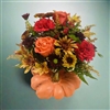Autumn bouquet with orange roses, red carnations, bronze poms, alstroemeria, and berries arranged in a ceramic pumpkin container.