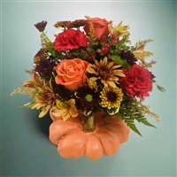 Autumn bouquet with orange roses, red carnations, bronze poms, alstroemeria, and berries arranged in a ceramic pumpkin container.
