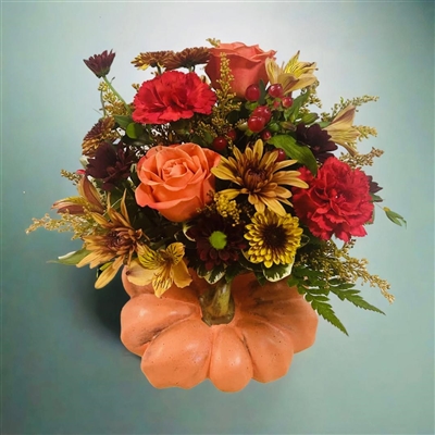 Autumn bouquet with orange roses, red carnations, bronze poms, alstroemeria, and berries arranged in a ceramic pumpkin container.