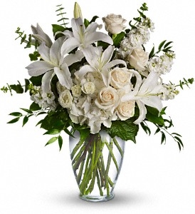 Tall all-white vase arrangement with hydrangea, roses, spray roses, stock, and eucalyptus in a clear vase.