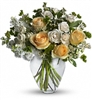 Celestial Love bouquet with yellow roses, cream spray roses, white stock, and waxflower in a clear glass vase