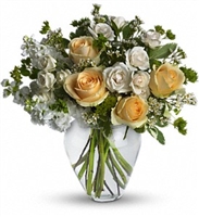 Celestial Love bouquet with yellow roses, cream spray roses, white stock, and waxflower in a clear glass vase