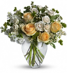 Celestial Love bouquet with yellow roses, cream spray roses, white stock, and waxflower in a clear glass vase