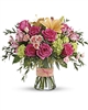 Bright bouquet with hot pink roses, peach lilies, green hydrangea, pink spray roses, alstroemeria, and eucalyptus in a glass gathering vase with a bow.