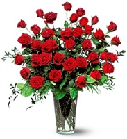 Three dozen long-stem red roses arranged in a tall clear glass vase with lush greenery.